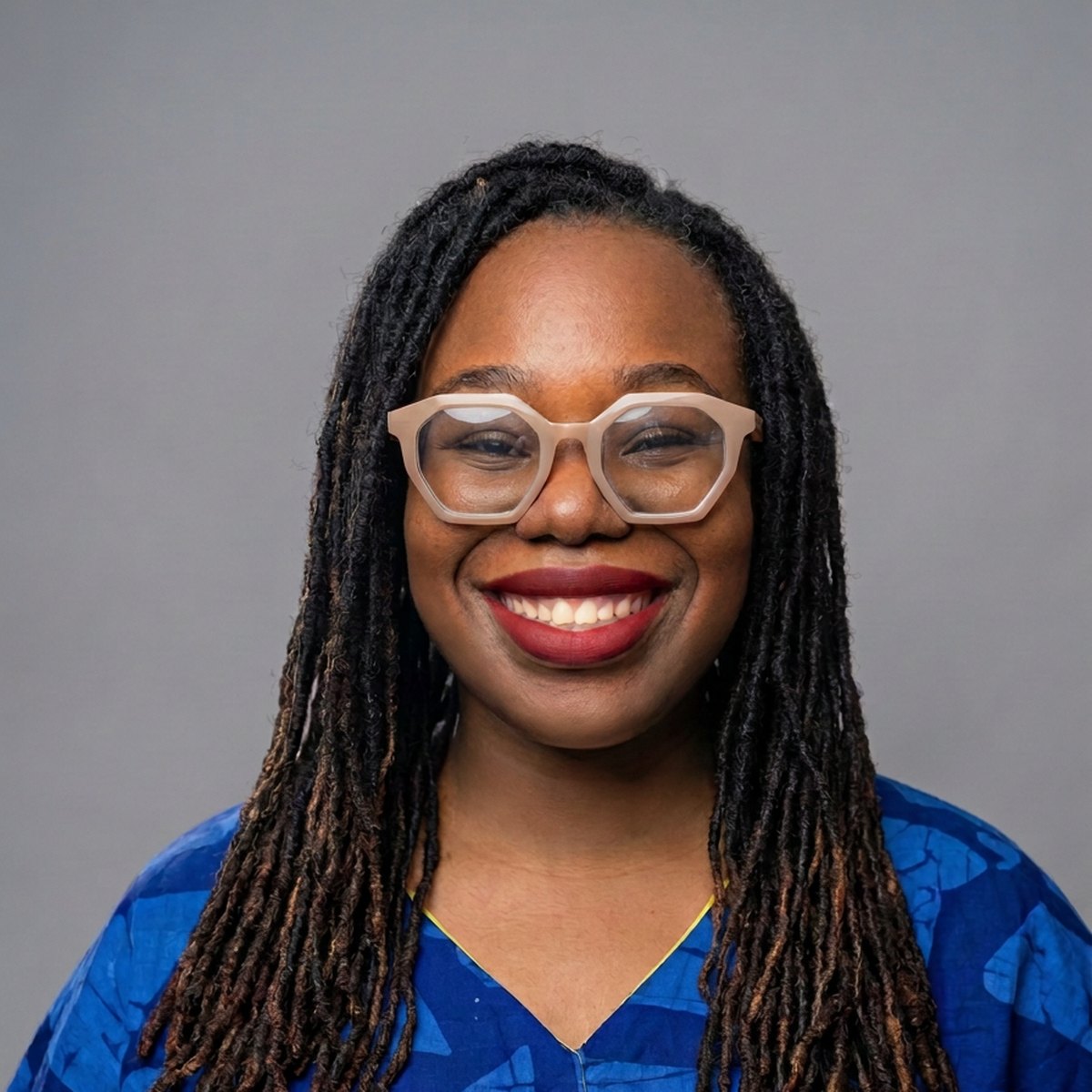 Nana Nwachukwu, souriante, avec des lunettes à monture claire et un haut bleu à motifs