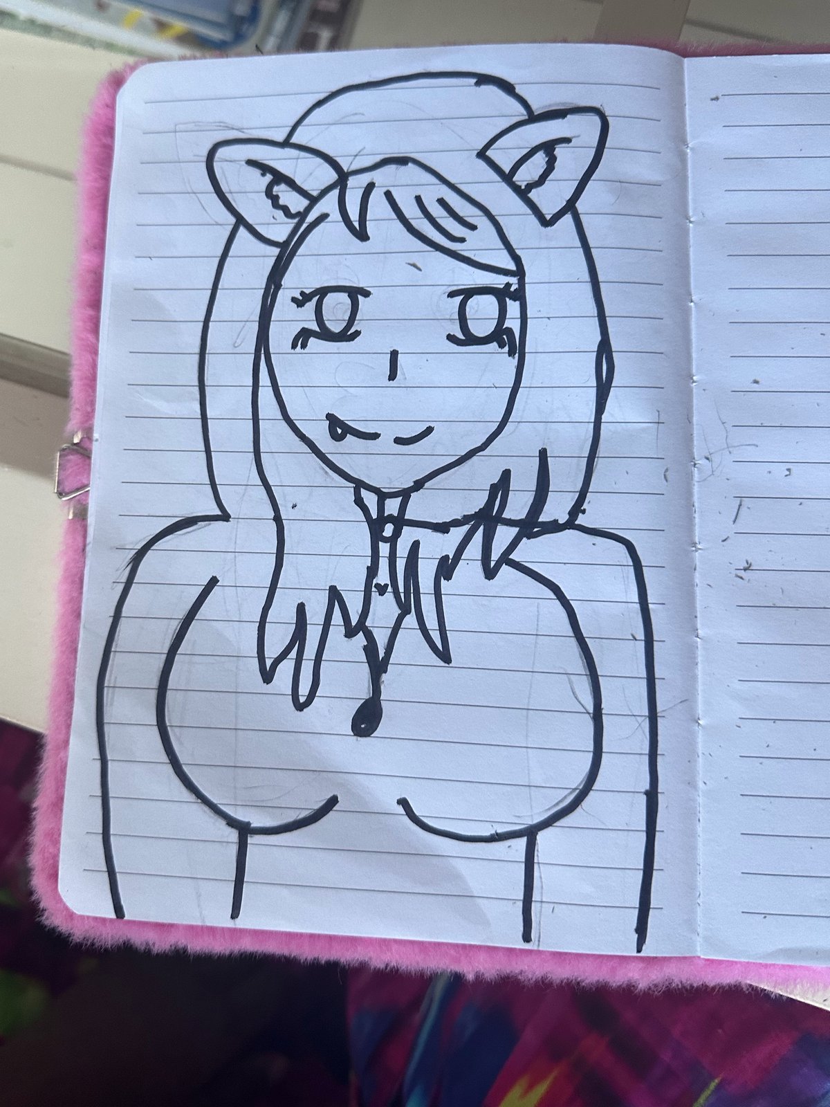 A black pen drawing of a smiling girl with long hair and cat ears, in a lined notebook with a fluffy pink cover.